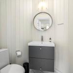 Badezimmer mit Toilette, Waschbecken und Spiegel an vertikal verkleideten Wänden.