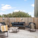 Terrasse mit Sitzgruppe, Tisch und Holzgeländer. Hintergrund: Bäume und blauer Himmel.