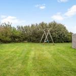 Grüner Garten mit Schaukel und Hecke. Holzwand rechts.