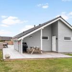 Ein graues Ferienhaus mit Terrasse, Grill und Picknicktisch. Grün umgeben.