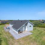 Ein hellblaues Haus mit Holzterrasse und Garten. Hintergrund: Grünflächen und andere Häuser.