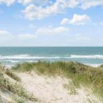 Sandpfad führt durch Dünen zur Ostsee mit Wellen und blauem Himmel.