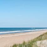 Strand mit Sanddünen und blauem Meer unter klarem Himmel.