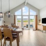 Wohn- und Essbereich mit Holzboden, großen Fenstern und TV. Terrasse mit Sitzmöbeln.