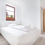 Schlafzimmer mit weißem Bett, Nachttisch und Fenster.