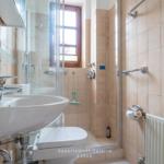 Badezimmer mit Dusche, Waschbecken und Toilette. Fenster mit Holzrahmen.