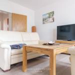 Wohnzimmer mit Sofa, Holztisch und Fernseher. Wandbild und Holztür sichtbar.