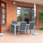 Terrasse mit Tisch, Stühlen und Sonnenschirm neben rotem Backsteinhaus