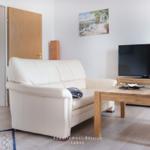 Wohnzimmer mit Sofa, Couchtisch und Fernseher. Wandbild und Holztüren sichtbar.