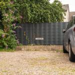 Ein silberner Wagen parkt auf Kies vor einem Zaun mit einer Pflanze und einem Schild.