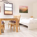 Schlafzimmer mit Bett, Tisch und Stühlen, Fenster und Wandbild.