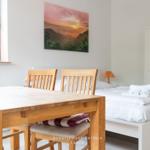 Schlafzimmer mit Bett, Tisch und Stühlen. Wandbild zeigt Sonnenuntergang.