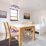 Ein Raum mit Tisch, Stühlen, Bett und Schränken. An den Wänden hängen Bilder.