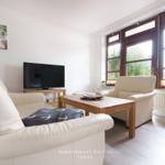 Wohnzimmer mit Sofa, Sessel, Fernseher und großen Fenstern.