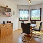 Esszimmer mit Tisch, Stühlen, Fenstern und Holzmöbeln.