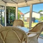 Terrassentisch mit drei Stühlen unter Glasdach. Blick auf Garten und Nachbarhäuser.