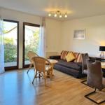 Wohnzimmer mit Sofa, Esstisch und Terrassentür. Holzboden und Fensterfront.