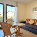 Wohnzimmer mit Sofa, Tisch und Stühlen. Durchgang zur Terrasse mit Blick auf Garten.