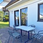 Terrasse mit Tisch und vier Stühlen vor weißem Haus mit Fenstern.