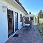 Terrasse mit Tisch und Stühlen neben Haus mit Glasveranda.