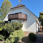 Wohnhaus mit Balkon, Garten und gepflastertem Weg unter blauem Himmel.