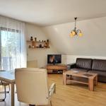 Wohnzimmer mit Sofa, TV und Essbereich. Holzboden und große Fenster.