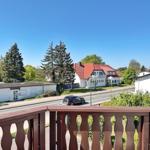 Blick vom Balkon auf Straße, Bäume und ein Haus mit rotem Dach.