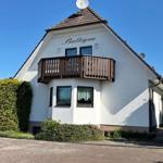 Weißes Haus mit Balkon und Satellitenschüssel unter blauem Himmel.