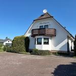 Weiße Villa mit Balkon und Satellitenschüssel unter blauem Himmel.