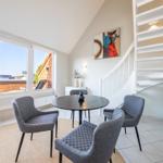 Essbereich mit runden Tisch und vier Stühlen. Weiße Treppe und große Fenster zur Terrasse.