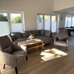 Wohnzimmer mit Sofa, zwei Sesseln und Holztisch. Durchgänge zu Essbereich und Terrasse.