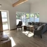Wohnzimmer mit Sofa, Sessel und Holzboden. Große Fenster und Holzbalken.