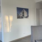 Wohnzimmer mit grauem Sessel und Wandbild. Küchenbereich links sichtbar.