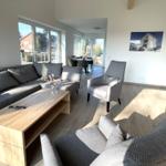 Wohnzimmer mit Sofa, Sessel und Holztisch. Durchgang zum Essbereich mit Tisch und Stühlen.