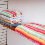 Farbige Handtücher liegen auf einem Holzregal. Ein weiteres Handtuch liegt daneben.