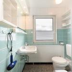 Badezimmer mit Waschbecken, Toilette und Dusche. Wandfliesen in Türkis und Weiß.