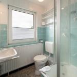 Badezimmer mit Dusche, Toilette und Waschbecken mit Fenster.