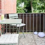 Terrasse mit Tisch, zwei Stühlen und zwei Luftballons. Hintergrund: Holzgeländer und grüne Bäume.