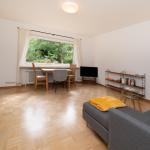 Wohnzimmer mit Sofa, Esstisch und TV. Holzboden und Fenster mit Blick auf Grün.