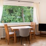 Esszimmer mit Tisch, Stühlen und TV. Große Fenster mit Blick auf Bäume.