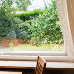 Durch das Fenster blickt man auf einen grünen Garten mit Bäumen und einem weißen Stuhl.