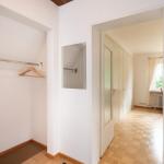 Flur mit Kleiderschrank, Spiegel und Tür zu einem Zimmer mit Holzboden.