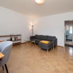 Wohnzimmer mit Sofa, Tisch und Bücherregal. Holzfußboden und Tür zum Bad.