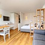 Wohnbereich mit Sofa, Bett und Esstisch. Holzboden und weiße Wände.