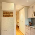 Küche mit weißen Schränken und Holzakzentwand. Durchgang zu Wohnbereich mit Holzboden.