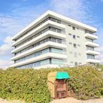 Moderne Mehrfamilienhaus mit Balkonen und Strandhütte im Vordergrund.