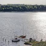Bootshafen mit zwei Booten an Steg und grüner Uferlinie im Hintergrund.