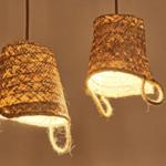 Zwei hängende, geflochtene Lampenschirme aus Naturmaterial mit Lichtquellen darin.