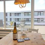 Holztisch mit Weinglas und Flasche vor großem Fenster mit Blick auf Balkon und Wasser.