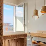 Essbereich mit Holztisch, Bänken und Hängelampen. Blick auf Balkon mit Stadtblick.